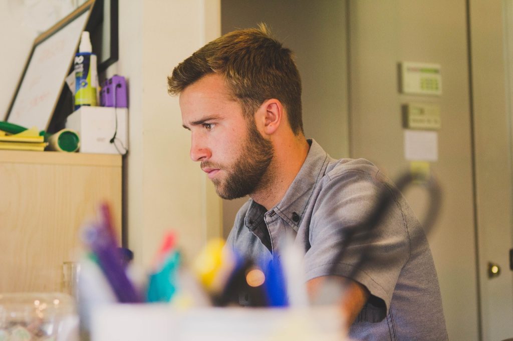 Man focusing intently on computer screen at work in an office setting with blurred foreground pens and office supplies