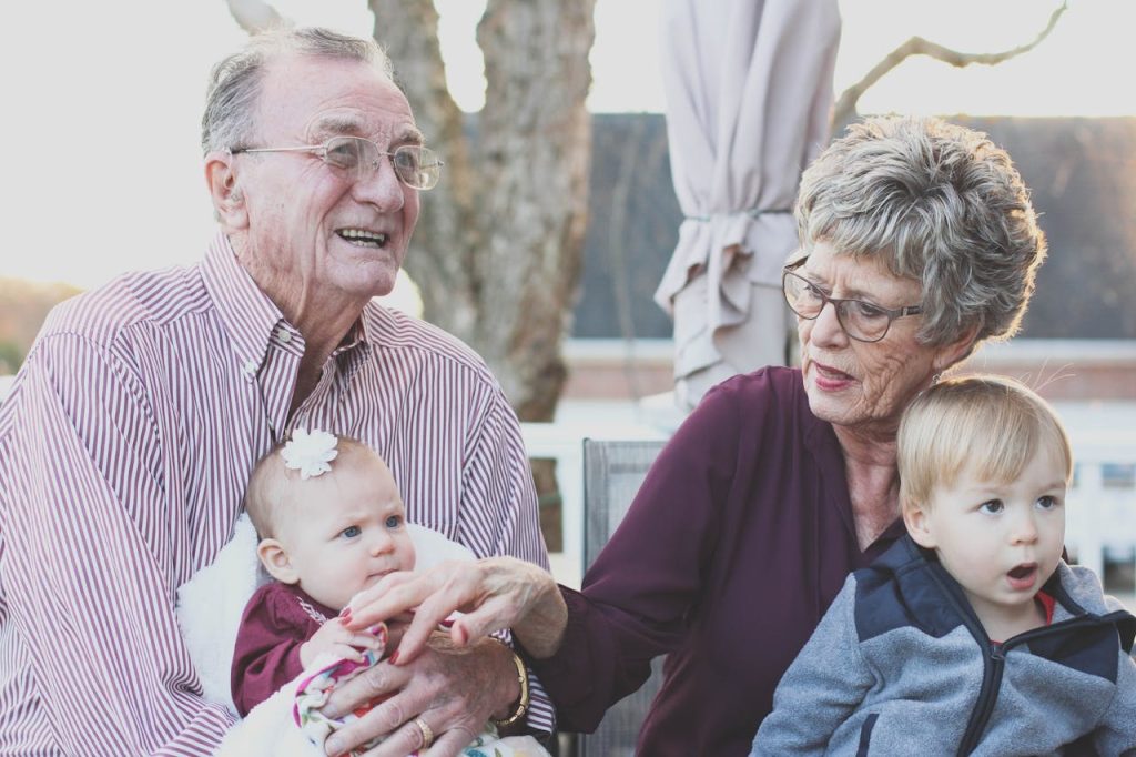 Elderly couple enjoying time with their two grandchildren outdoors in a garden setting