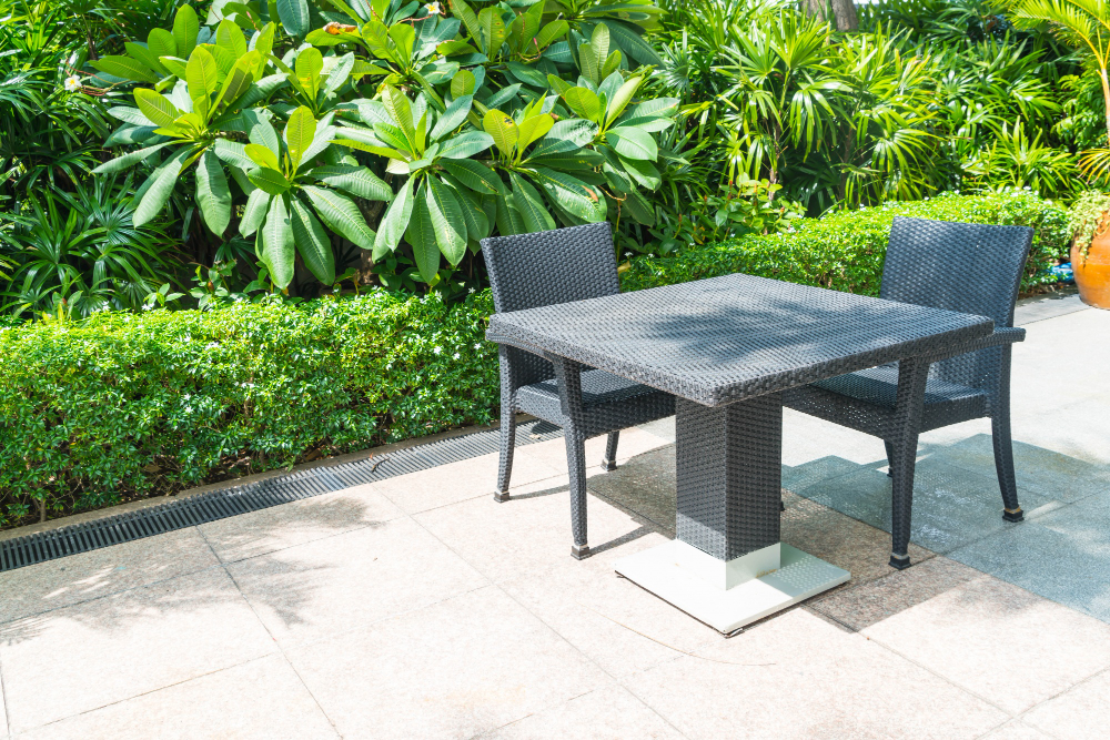 Outdoor patio with wicker table and chairs, surrounded by lush greenery for a relaxing garden setting